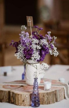 purple and white flowers in a mason jar on a wooden slice at a wedding reception