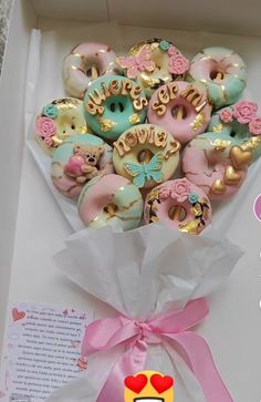 a box filled with lots of donuts covered in pink and blue icing next to a ribbon