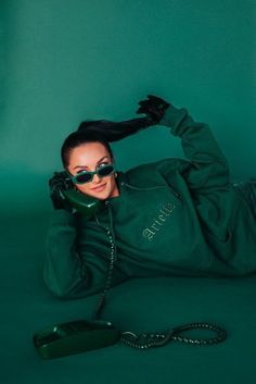 a woman laying on the ground with her hands behind her head, wearing sunglasses and a green hoodie