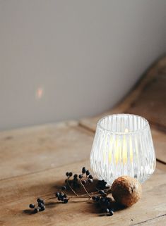 a glass candle holder sitting on top of a wooden table next to an acorn