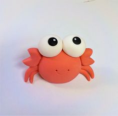 a close up of a plastic crab on a white surface with one eye open and the other half closed