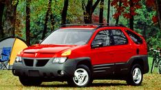 a red car parked next to a tent in the woods