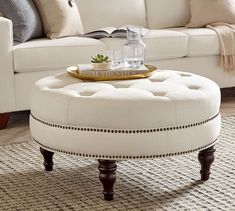 a white ottoman sitting on top of a rug next to a couch and coffee table