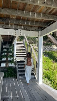 a woman in white is walking down the stairs to her beachside house with plants on either side