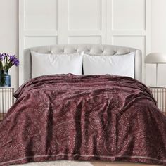 a bed covered in a maroon blanket and pillows