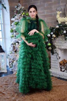 a woman in a green dress standing next to a christmas tree