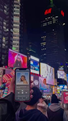 a person holding up a cell phone in the middle of a busy city at night