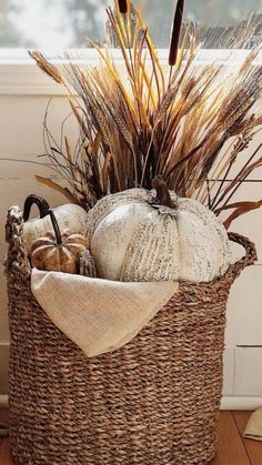 a basket filled with lots of different types of pumpkins and grass in it on top of a wooden floor