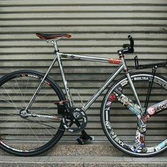 a silver bicycle parked next to a wall with graffiti on it's front wheel