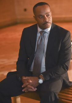 a man in a suit and tie sitting on a wooden bench with his hands crossed