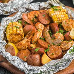 shrimp, corn on the cob and potatoes in foil with lemon wedges next to it