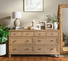 a wooden dresser sitting next to a large mirror and potted plant on top of it