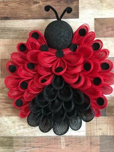 a red and black wreath with a lady bug on it's back, sitting on a wood floor