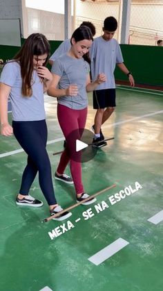 two girls are playing with a skateboard in an indoor gym while another girl watches