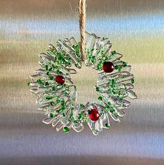 a glass ornament hanging from a rope on a metal surface with green and red beads