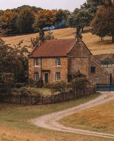 an old brick house in the middle of a field with trees and grass around it