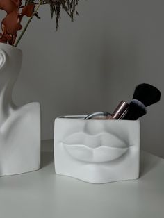 two white vases sitting on top of a table with makeup brushes and brushes in them