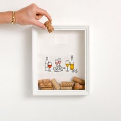 a hand is holding a cork and some wine glasses in a white frame on the wall