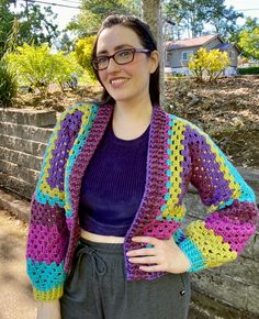 a woman standing next to a brick wall wearing glasses and a crocheted jacket