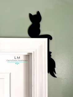 a black cat is sitting on top of a white door and it's shadow appears to be in the frame