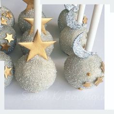 cake pops decorated with gold stars and moon on white frosted balls, next to candles