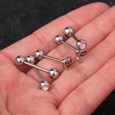 three pairs of surgical steel nose studs with pink and silver balls on them in a person's hand