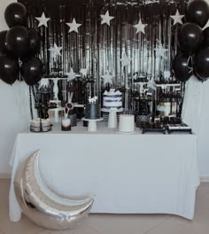 a table topped with black and white cake next to silver foil balloons in the shape of stars