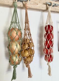 three hanging bags filled with onions and potatoes next to a hook on a white wall