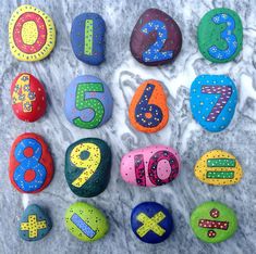 colorful painted rocks with numbers and symbols on them sitting on a marble surface in the shape of letters