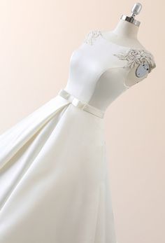 a white dress on a mannequin with a flower in the center and a bow at the waist