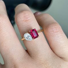 a woman's hand holding an engagement ring with two diamonds on it and a pink tourmaline in the middle