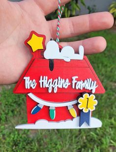 a hand holding a red house ornament with the words, the hugup family on it