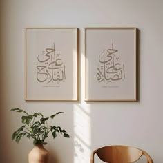 two framed arabic art prints on the wall above a table with a potted plant