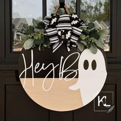 a door hanger with a ghost on it that says heaffs and is decorated with greenery