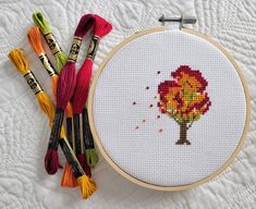 the cross stitch tree is next to some crochet hooks and threads on a white surface