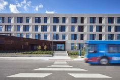 a blue bus driving past a tall building on a street with white crosswalks