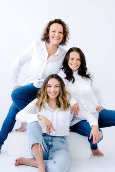 three women sitting on top of each other in front of a white wall and posing for the camera