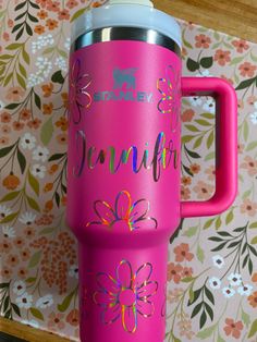 a bright pink tumbler with the words january painted on it and flowers in the background