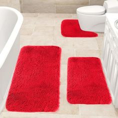 three red rugs in a bathroom next to a white toilet and bathtub with the lid open