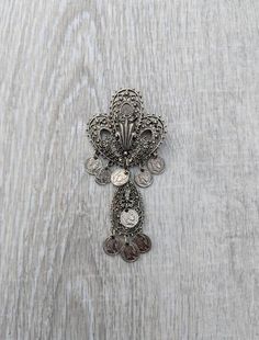 This gorgeous Arthur Pepper brooch exhibits all the characteristics of the Midcentury Etruscan Revival period in jewelry design. It features a large, incredibly intricate silver tone fleur-de-lis, its openwork lines crisscrossed with repeated geometric patterns and dotted with tiny spheres. Both the classic French three-pronged lily and the teardrop shaped framework that dangles below it are adorned with replicas of Emperor Napoleon coins. The early 19th Century francs show the ruler's bust in p Vintage Ceremonial Pendant Brooches, Vintage Ceremonial Pendant Brooch, Vintage Pendant Brooches For Ceremonial Occasions, Emperor Napoleon, Hat Brooch, Leprechaun Hats, Enamel Flower, Schmuck Design, White Enamel