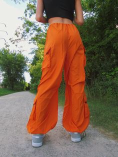 These bright orange cargo/parachute pants are the coolest Fall and Winter wardrobe staple. Featuring 4 pockets, an adjustable drawstring cord waistline, and adjustable cord drawstring ankles. Emily is wearing size S. Summer Hiking Cargo Pants With Pockets, Summer Cargo Pants With Pockets For Hiking, Summer Hiking Cargo Pants With Cargo Pockets, Summer Utility Parachute Pants For Outdoor Activities, Summer Hiking Pants With Cargo Pockets, Summer Hip Hop Cargo Style Parachute Pants, Nylon Cargo Pants For Summer Hiking, Summer Nylon Cargo Pants For Hiking, Summer Hip Hop Parachute Pants With Cargo Pockets