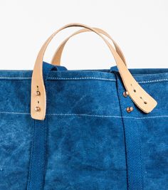 a blue canvas bag with leather handles on a white background, showing the bottom part of the bag