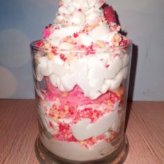 a dessert in a glass is topped with white and pink sprinkles on a table