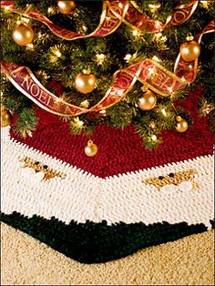 a knitted christmas tree skirt with gold and red ornaments on it, next to a decorated christmas tree