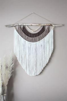 a wall hanging with beads and feathers on it next to a vase filled with flowers