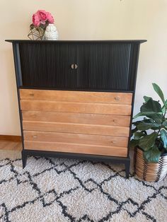 a wooden dresser sitting on top of a rug next to a potted plant in a vase