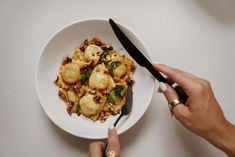 a person holding a knife and fork over a plate of food on a white table