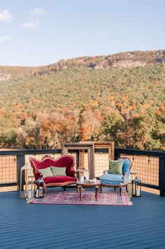 two chairs and a couch on a deck with mountains in the background