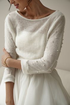 a woman in a white dress and pearls on her arm wearing a pearled sweater