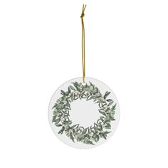 a white ornament with green leaves hanging from a gold string on a white background